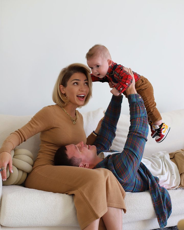 Mom laughing while dad lifts their baby son in the air on the family couch