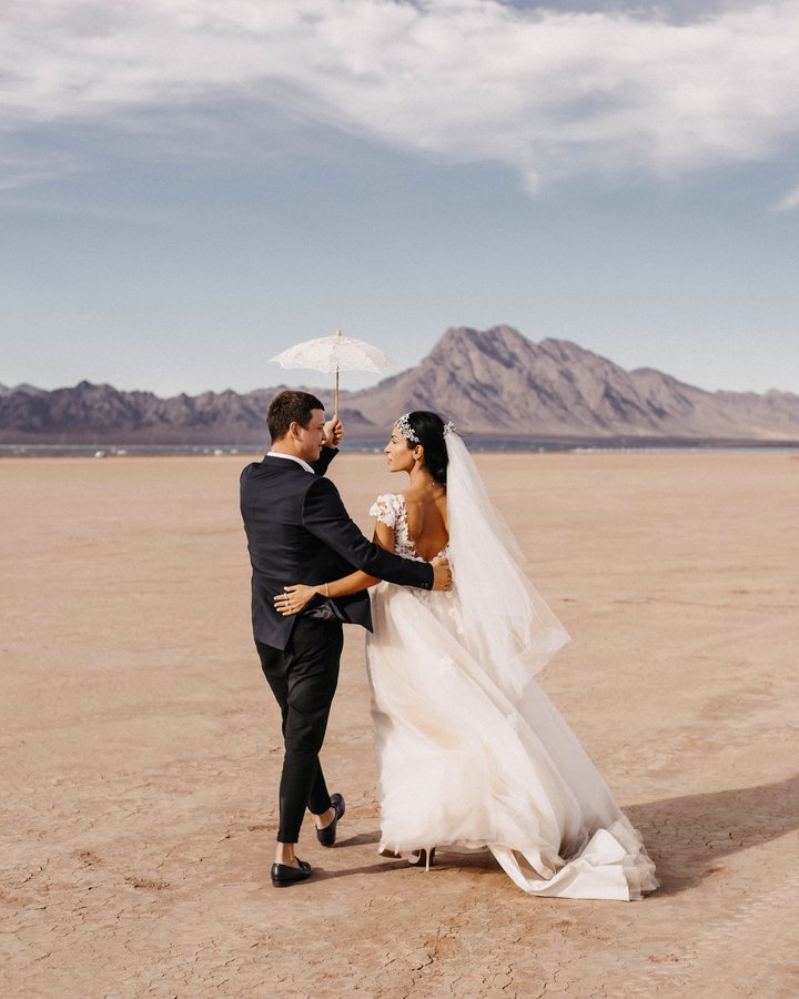 The founders on their wedding day, walking across a desert with a lace parasol